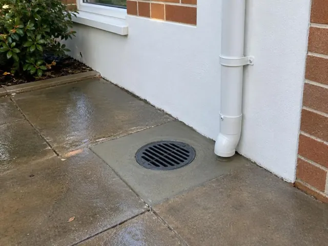 Outdoor drain grate beside wet paved patio and house wall in Bellbird