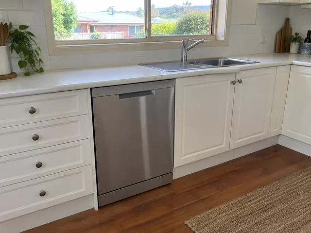 Built-in dishwasher under a kitchen benchtop beside a sink and window in a white kitchen in Cessnock