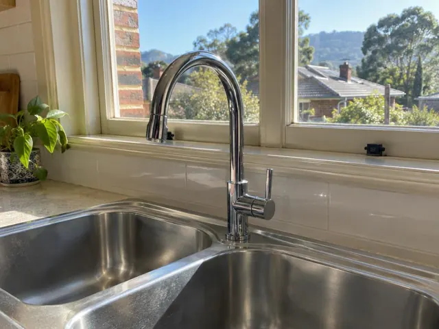 Chrome kitchen mixer tap above a stainless steel double sink with tiled splashback and window view in Aberdare