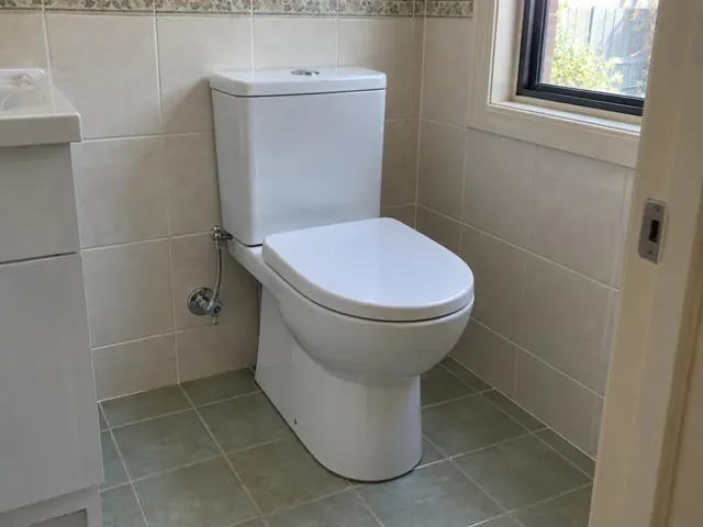 White toilet beside tiled wall and window in a beige bathroom in Mount View